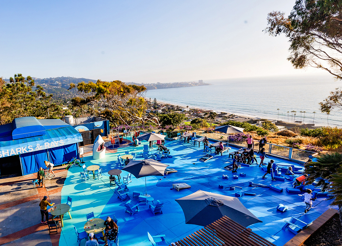 A scenic view overlooking people playing on Blue Beach, with the ocean visible in the distance under a bright sky.