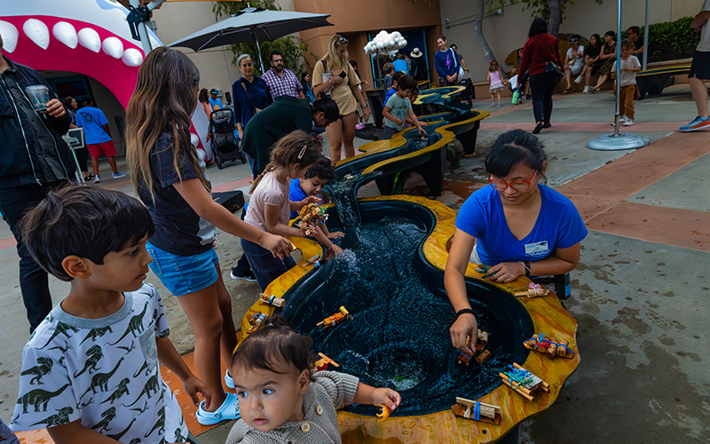 Children engage in a hands-on water-play experience, interacting with a flowing miniature river.