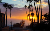 Colorful sunset over Scripps Pier with silhouettes of palm trees.