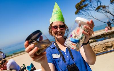 Aquarium worker in blue shirt and party hat holds up specimen jars.