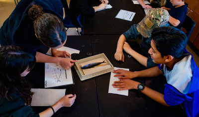 Four students gathered around a table, closely examining a fish during a hands-on dissection activity.