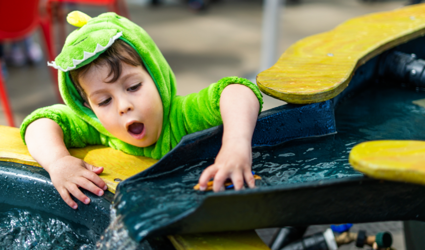 a child with an excited expression plays in the running water in a Riveropolis exhibition 