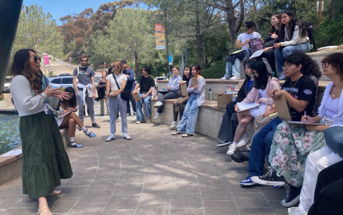 students sit beside the aquarium's Whale Fountain while their instructor talks